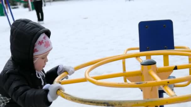 Linda niña balanceándose en el patio de recreo en el frío día nevado en invierno — Vídeos de Stock