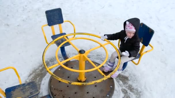 Schattig klein meisje swingende op speelplaats op koude besneeuwde dag in de winter — Stockvideo