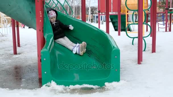 Söt liten flicka gungar på lekplats på kall snöig dag i vinter — Stockvideo