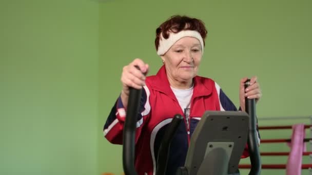 Uma mulher idosa em um treinador elíptico em um ginásio 4k — Vídeo de Stock