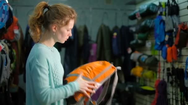 Молодая девушка консультант в специализированном магазине для туризма выбирает рюкзак . — стоковое видео