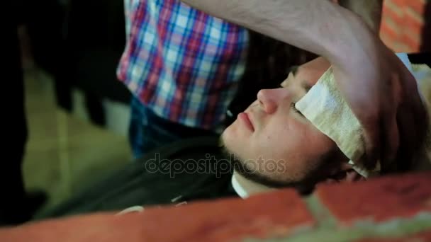 Вид зверху на обличчя людини, що спирається на голову назад у раковину із закритими очима, коли перукар миє волосся повільно — стокове відео