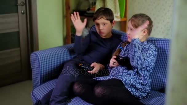 Dość mała dziewczynka i chłopiec są gry konsoli do gier i śmiejąc się siedząc na kanapie w domu dobre — Wideo stockowe