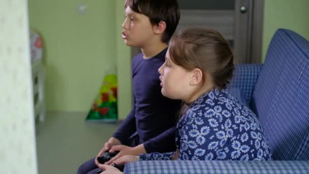 Pretty little girl and boy are playing game console and laugh while sitting on sofa at home good — Vídeos de Stock