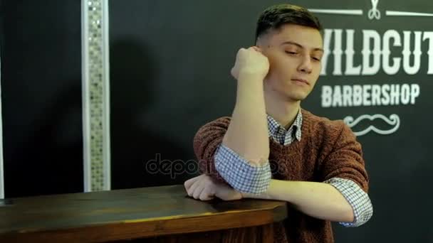 Tijd voor een nieuw kapsel. Knappe jonge bebaarde man kijken naar zijn spiegelbeeld in de spiegel en daarbij hand in haar zittend in stoel barbershop beste — Stockvideo