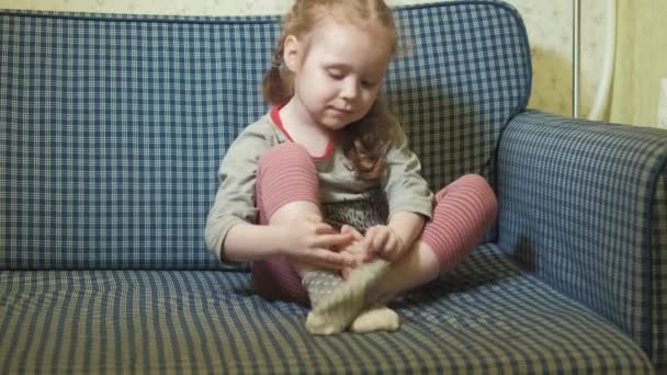 Маленькая девочка одевает носки сидя на диване 4k — стоковое видео