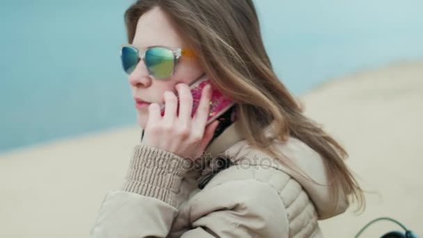 Mulher bonita sentada perto do mar e segurando seu telefone 4k — Vídeo de Stock