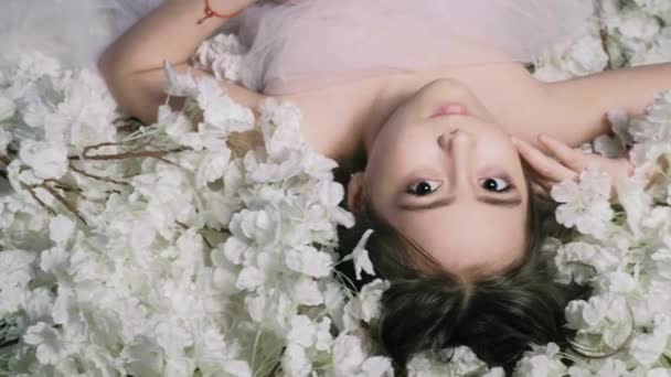 Hermosa chica se encuentra en las flores y sonrisas, en el interior 4k — Vídeo de stock