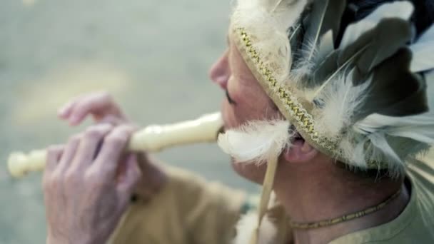 Een Indiaan in een nationale kostuum speelt een fluit in de buurt van een boot op de rivier bank 4k — Stockvideo