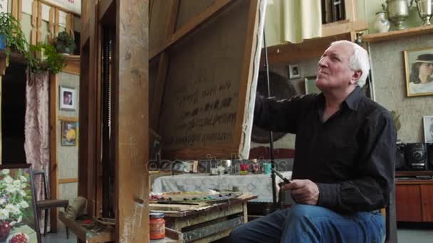 Пожилой художник пишет картину в своей студии 4k — стоковое видео