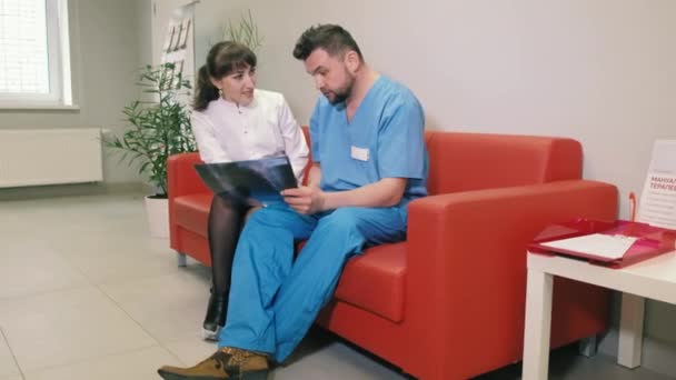 医師二人、男と女は診療所でソファーに座っているとお互いに話しています。4 k — ストック動画