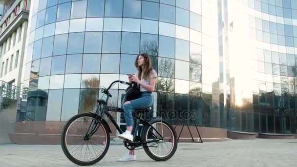 Mulher bonita monta uma bicicleta perto de um edifício alto 4k — Vídeo de Stock