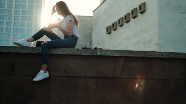 Bruna ragazza in occhiali si siede al tramonto ascolta la musica raddrizza i capelli — Video Stock