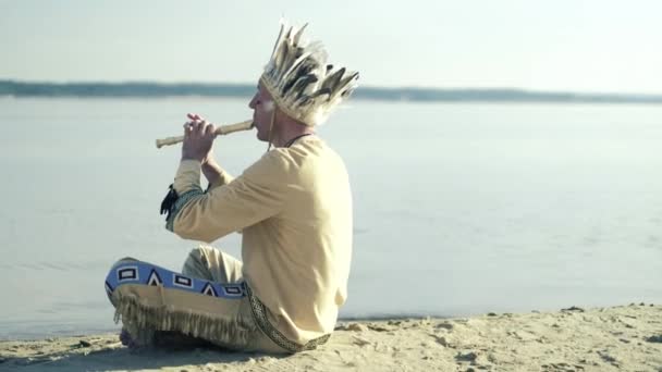 Un indian într-un costum național cântă la flaut pe malul râului 4k — Videoclip de stoc