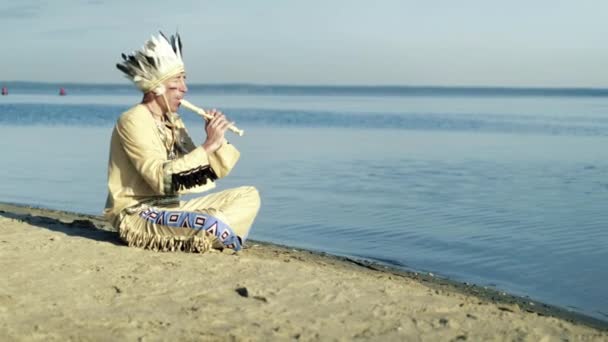 Indián v národním kroji hraje na flétnu na břehu řeky 4k — Stock video