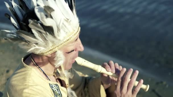 Indián v národním kroji hraje na flétnu na břehu řeky 4k — Stock video