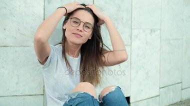 Şehrin gri ceket sokak tuğla duvara yakın duran güzel moda kadın. Uzun saçlı ve gözlüklü duvarının yakınında esmer seksi kızla kamera dikkat et. 4k