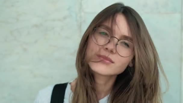 Hermosa mujer de moda de pie cerca de la pared de ladrillos en la calle de la ciudad en abrigo gris. Morena chica sexy con el pelo largo y gafas cerca de reloj de pared en la cámara. 4k — Vídeos de Stock