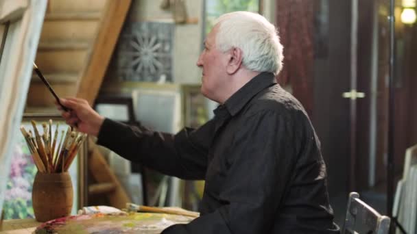 En äldre konstnär skriver en bild i sin studio 4k — Stockvideo