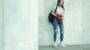 Esmer kız bir zemin mermer bir gri duvar üzerine gelmek ile bir sırt çantası ve ellerini ve telefon görüşmeleri bir ceket veya müzik dinliyor