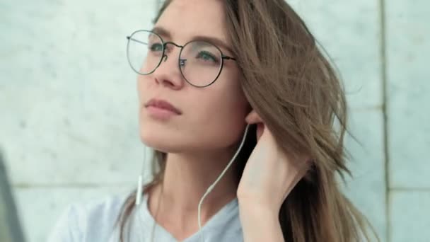 Hermosa chica morena en gafas sobre un fondo de mármol gris pared incluida música agradable y disfruta — Vídeo de stock