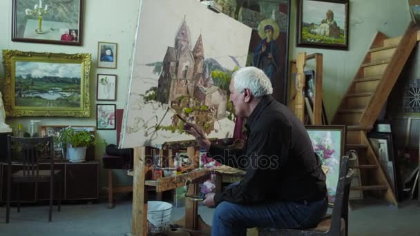 Un artista de edad avanzada escribe una foto en su estudio 4k — Vídeo de stock