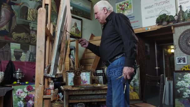 An elderly artist writes a picture in his studio 4k — Stock Video