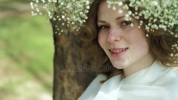 Hermosa mujer en un vestido blanco en el bosque con flores 4k — Vídeos de Stock