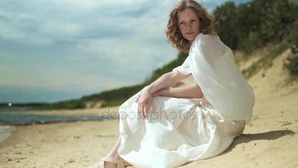 Mujer en vestido blanco que permanece en una playa con flor en el día soleado 4k — Vídeos de Stock