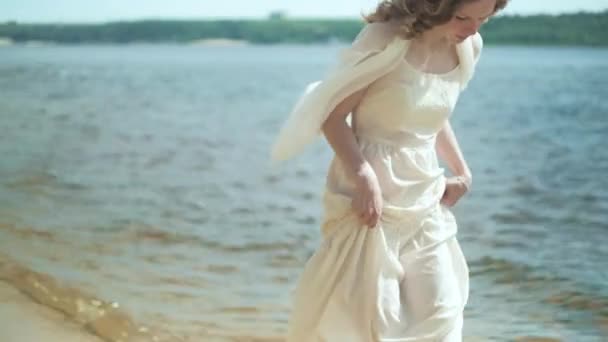 Mujer en vestido blanco que permanece en una playa con flor en el día soleado 4k — Vídeo de stock