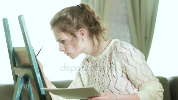 Mulher artista em um cavalete desenha uma flor ao lado de uma borboleta senta-se 4k — Vídeo de Stock