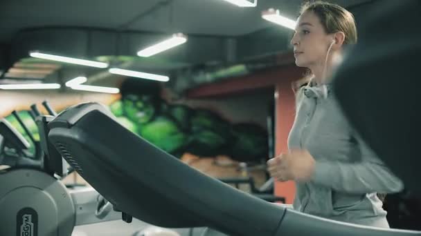 Chica atractiva corriendo en una cinta de correr en el gimnasio 4k — Vídeo de stock