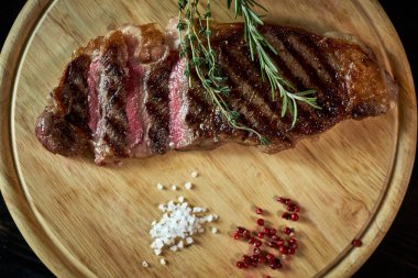 Biberiye ve baharatlar ile rustik kesme tahtası üzerinde orta az pişmiş ızgara biftek dilimlenmiş, karanlık rustik metal arka plan üstten görünüm, yerleştirmek için metin jpg