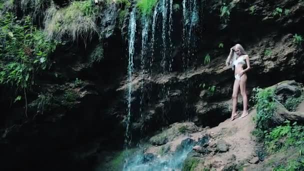 Bela mulher em um biquíni de pé perto de uma cachoeira — Vídeo de Stock