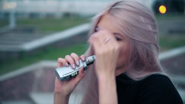 Joven hermosa mujer con maquillaje de moda al aire libre con un vapor de cigarrillo electrónico 4k — Vídeos de Stock