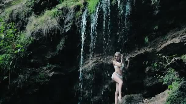 Schöne Frau im Bikini, die in der Nähe eines Wasserfalls steht — Stockvideo