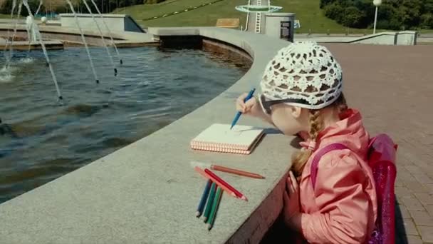 Vacker flicka ritar i en anteckningsbok nära fontänen — Stockvideo