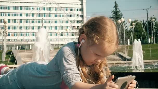 漂亮的女孩在喷泉附近的手机耳机上听音乐 — 图库视频影像