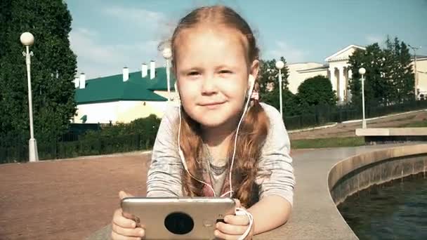 Schönes Mädchen hört Musik über Kopfhörer mit Handy in der Nähe des Brunnens — Stockvideo
