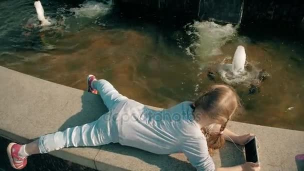 Vacker flicka Lyssna på musik i hörlurar med telefon nära fountain — Stockvideo