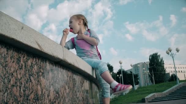 Mooi meisje lollipop eten in de buurt van een fontein op een heldere dag — Stockvideo