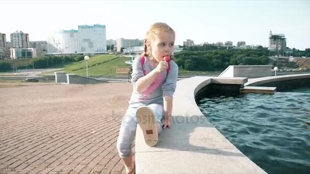 Hermosa chica comiendo piruleta cerca de una fuente en un día brillante — Vídeos de Stock