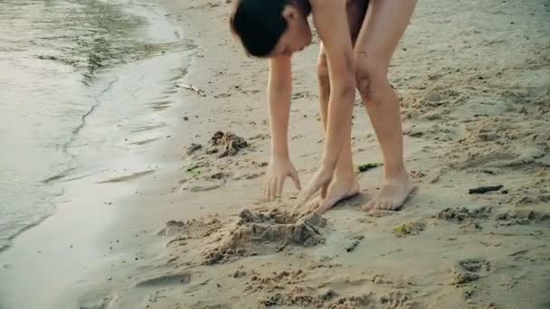 Liten pojke spelar på stranden i sanden. Barn skulpterar figurer ur sanden. Aktiviteter på sommaren på havet. — Stockvideo