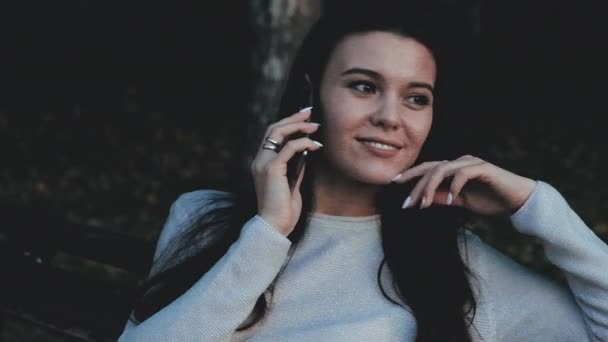 Uma bela jovem profissional está tendo uma conversa telefônica, ao ar livre na cidade à noite. Ela está sorrindo. — Vídeo de Stock