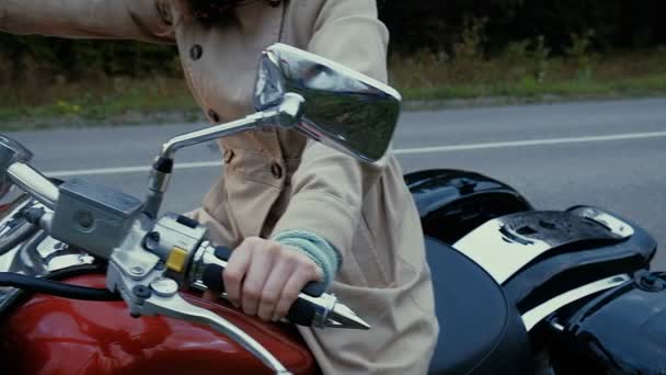Jovem com cabelo castanho senta-se em uma moto perto de uma estrada . — Vídeo de Stock