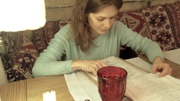 Vrouw in een café. Vrouw kijkt naar het menu in een café — Stockvideo