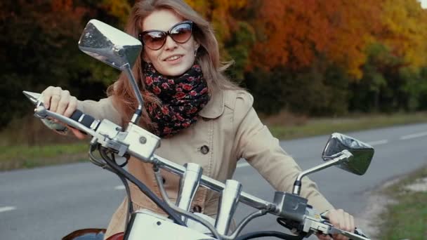 Chica joven con el pelo castaño se sienta en una moto cerca de una carretera . — Vídeos de Stock