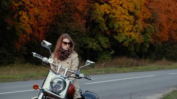 Молодая девушка с каштановыми волосами сидит на мотоцикле возле дороги . — стоковое видео