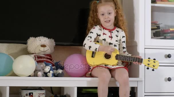 Małe dziecko grając ukulele na kanapie — Wideo stockowe