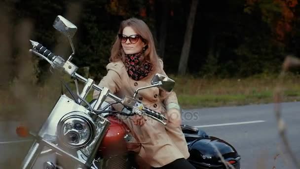 Молода дівчина з коричневим волоссям сидить на мотоциклі біля дороги . — стокове відео